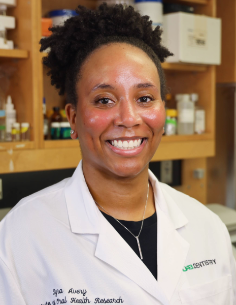 Woman with black hair wearing a white coat smiling in a lab setting
